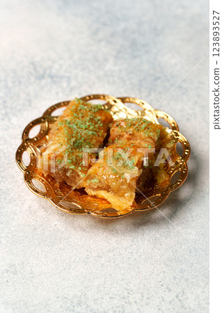 Delicious baklava served on a decorative golden plate with green pistachio garnish at a cozy cafe setting 123893527