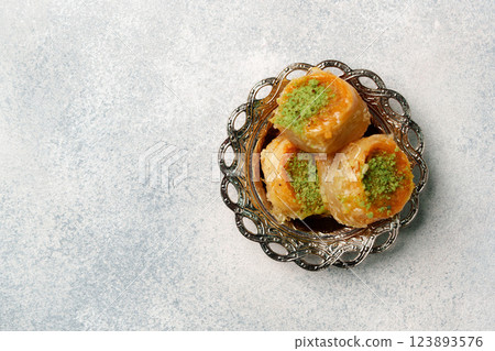 Delicious baklava garnished with pistachios served in an ornate dish on a textured background 123893576