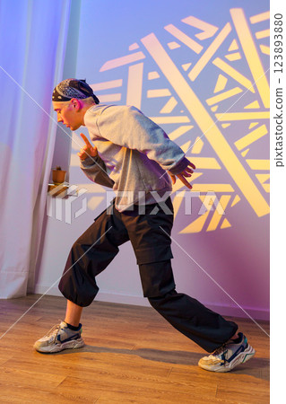 A young man dances in a studio with a geometric light projection on the wall A young man dances in a studio with a geometric light projection on the wall 123893880