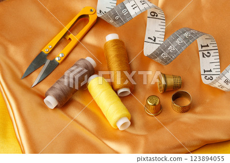 Sewing tools and materials arranged on a luxurious golden fabric background in a creative crafting workspace 123894055