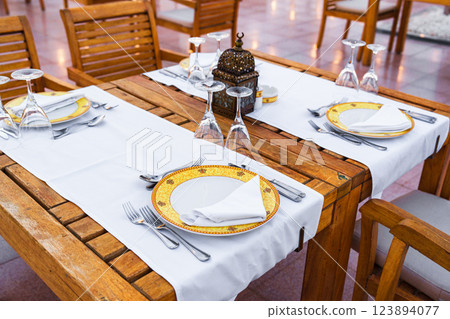 Elegant dining setup in an outdoor restaurant with wooden furniture and delicate tableware during a sunny afternoon 123894077