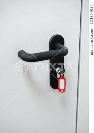 Key hanging on a red tag attached to a black door handle on a plain white door in a modern setting Key hanging on a red tag attached to a black door handle on a plain white door in a modern setting 123894083