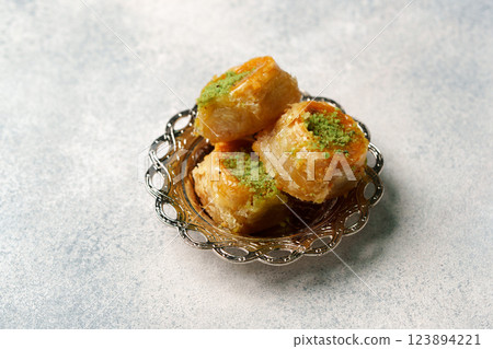 Delicious layers of baklava topped with crushed pistachios served in a decorative bowl on a soft gray surface Delicious layers of baklava topped with crushed pistachios served in a decorative bowl on a soft gray surface 123894221