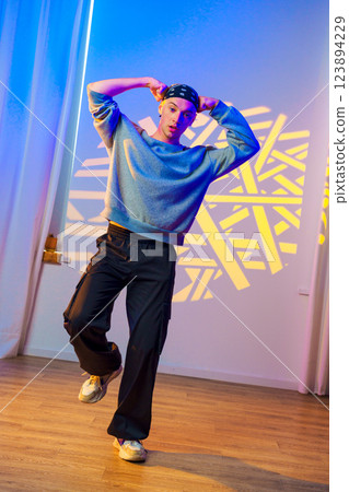 A young man dances in a studio, his movements accentuated by the colorful lights and geometric patterns projected on the wall A young man dances in a studio, his movements accentuated by the colorful lights and geometric patterns projected on the wall 123894229