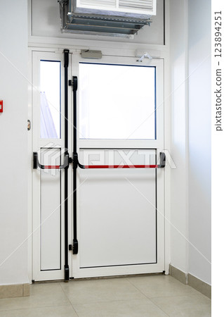 Modern double door with red safety bar in a clean, well-lit hallway of a building 123894251