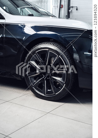 Car with sleek black alloy wheels showcased in a modern garage setting during daylight hours Car with sleek black alloy wheels showcased in a modern garage setting during daylight hours 123894320