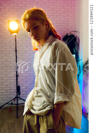 Young person in an artistic studio with colorful lighting showcases a modern fashion style during a creative session Young person in an artistic studio with colorful lighting showcases a modern fashion style during a creative session 123894321