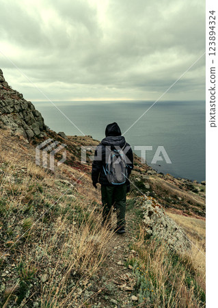 Hiker explores rugged coastline under moody skies near the ocean Hiker explores rugged coastline under moody skies near the ocean 123894324