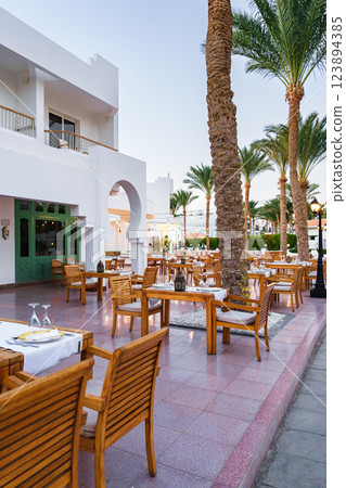 Outdoor dining area with wooden tables and palm trees at a resort during blue hour in a warm climate Outdoor dining area with wooden tables and palm trees at a resort during blue hour in a warm climate 123894385