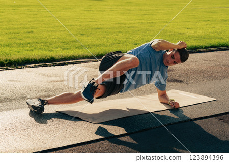 Man performing a plank exercise on a mat in a grassy outdoor area during daylight Man performing a plank exercise on a mat in a grassy outdoor area during daylight 123894396