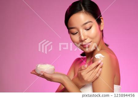 Woman applying body cream with a joyful expression in a vibrant pink background Woman applying body cream with a joyful expression in a vibrant pink background 123894456