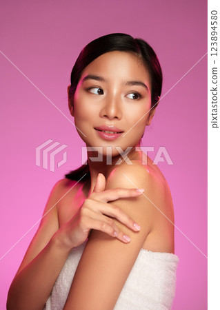 Young woman with glowing skin poses gracefully against a pink background during a beauty shoot 123894580