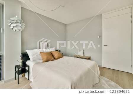 A stylish modern bedroom featuring a neutral color palette with a bed, elegant decor, and natural light flooding in through large windows. 123894621