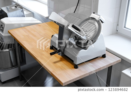 Slicing machine placed on a wooden table in a bright kitchen workspace Slicing machine placed on a wooden table in a bright kitchen workspace 123894682