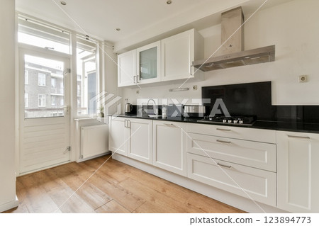A modern kitchen featuring white cabinetry, a black countertop, and ample natural light from large windows, creating a stylish and functional space. 123894773