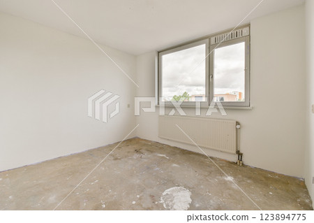 A spacious, uncluttered room featuring white walls and a large window, allowing natural light to flood in. The floor is bare, showcasing a minimalist aesthetic. 123894775