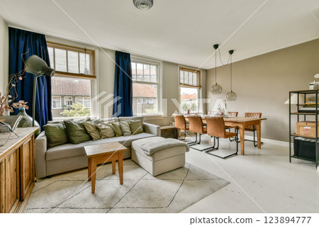 A stylish modern living room showcasing a comfortable sofa, wooden coffee table, and elegant dining area with contemporary lighting and decor. 123894777