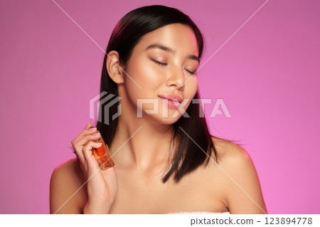 Model demonstrating skincare product application in a bright pink studio setting 123894778