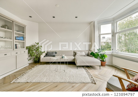 A contemporary living room featuring a minimalistic design with natural light, a cozy sofa, plants, and a stylish coffee table, creating an inviting space. 123894797