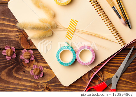 Crafting materials arranged on a wooden table along with a notebook and scissors for creative projects 123894802