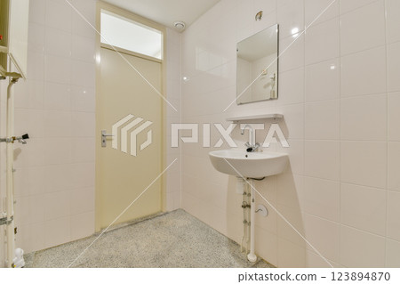 A sleek and tidy bathroom featuring white tiles, a simple mirror, and a compact sink design. Ideal for contemporary and minimalist aesthetics. 123894870