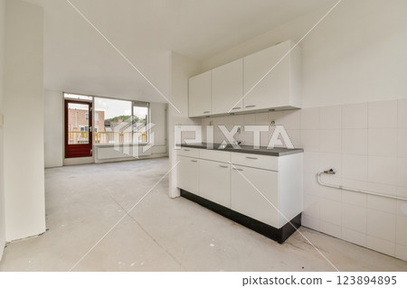 Spacious and minimalistic kitchen design with white cabinets and gray countertops, featuring unfinished flooring and large windows for natural light. Spacious and minimalistic kitchen design with white cabinets and gray countertops, featuring unfinished flooring and large windows for natural light. 123894895