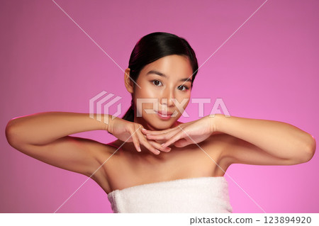Confident young woman posing with hands under chin in front of pink background during a beauty shoot Confident young woman posing with hands under chin in front of pink background during a beauty shoot 123894920