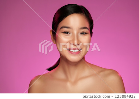 Smiling woman with natural makeup posing confidently against a vibrant pink background Smiling woman with natural makeup posing confidently against a vibrant pink background 123894922