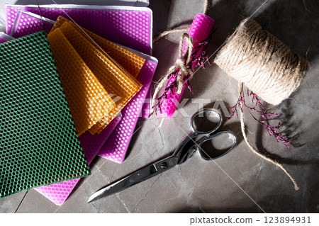Colorful wax sheets with scissors twine and wrapped candle on a stone surface 123894931