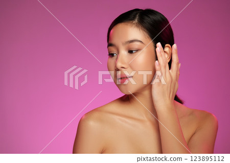 Woman posing with hand on face against a vibrant pink background during a beauty photoshoot Woman posing with hand on face against a vibrant pink background during a beauty photoshoot 123895112