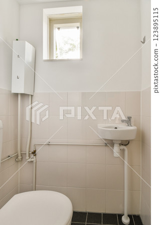 A clean and minimalistic bathroom featuring white tiles, a small window, and essential sanitary fixtures in a well-lit space. 123895115