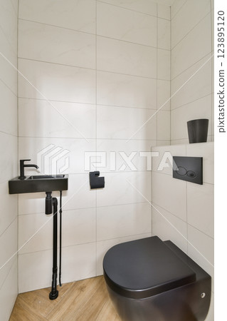 A sleek and contemporary bathroom featuring a black toilet and sink, complemented by minimalist tiles and a wooden floor for an elegant aesthetic. A sleek and contemporary bathroom featuring a black toilet and sink, complemented by minimalist tiles and a wooden floor for an elegant aesthetic. 123895120