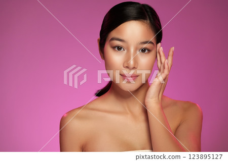 Woman with smooth skin touching her face against a pink background during a beauty shoot 123895127