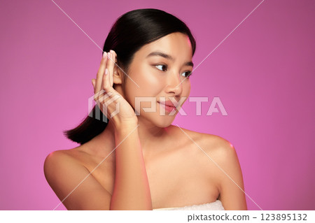 Woman applying skincare in front of a vibrant pink background during a beauty routine at home 123895132