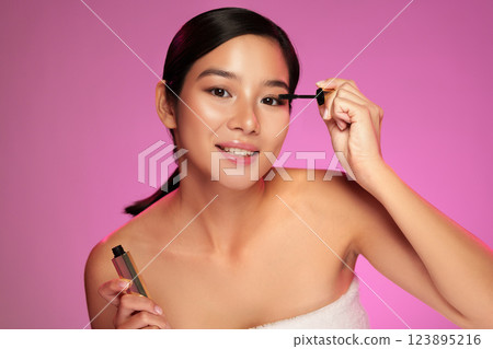 Model applies mascara in a beauty shoot with vibrant pink background showcasing makeup techniques Model applies mascara in a beauty shoot with vibrant pink background showcasing makeup techniques 123895216