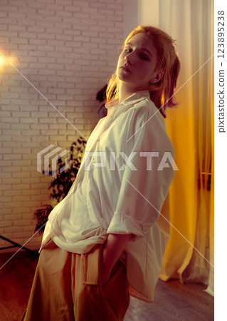 Stylish indoor portrait featuring a young woman with blonde hair and a relaxed pose in a softly lit room 123895238