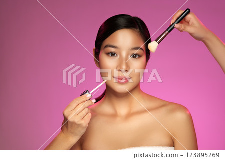 Makeup application with a focus on a model against a vibrant pink background during a beauty session in a studio Makeup application with a focus on a model against a vibrant pink background during a beauty session in a studio 123895269