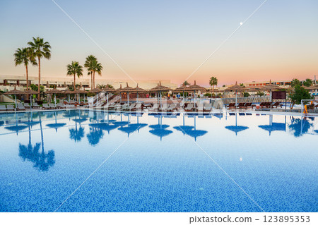 Relaxing evening at a tranquil poolside resort featuring palm trees and reflecting waters 123895353
