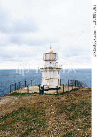 Lighthouse overlooking a calm ocean under a cloudy sky during the day near a coastal area 123895363