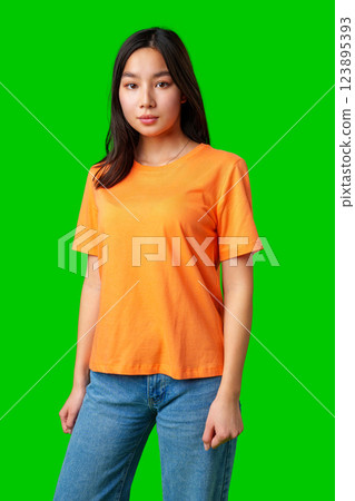 Young woman posing in bright orange t-shirt against green backdrop in a studio setting Young woman posing in bright orange t-shirt against green backdrop in a studio setting 123895393