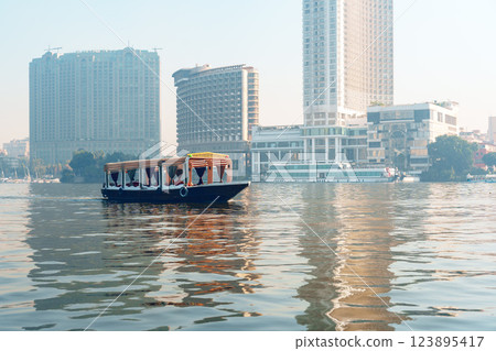Boaters enjoying a calm morning on the river beside modern buildings in a bustling city Boaters enjoying a calm morning on the river beside modern buildings in a bustling city 123895417