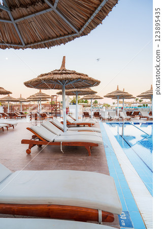 Relaxing sun loungers under straw umbrellas at a tranquil beachfront resort in the early evening 123895435