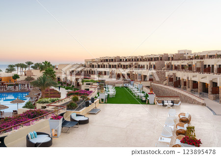 Elegant resort courtyard at sunset showcasing lush gardens and inviting lounge areas near the swimming pool 123895478