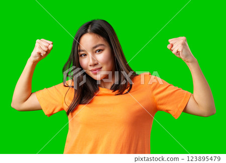 Confident girl shows strength wearing orange shirt against bright green background 123895479