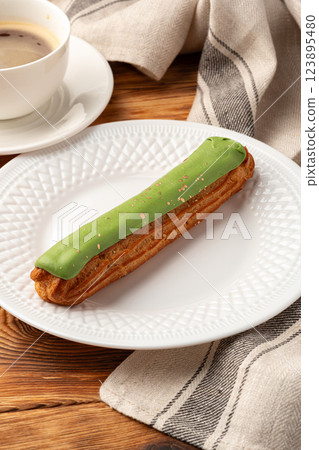 Delicious matcha eclair served on a white plate next to a cup of coffee at a cozy cafe 123895480