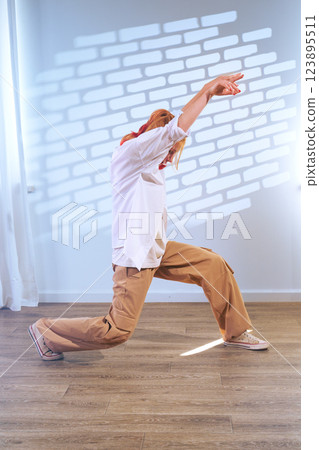 Dancer expresses creativity in a bright studio with wooden flooring and contrasting light patterns 123895511