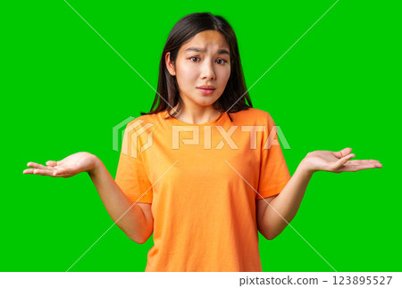 Young woman in an orange shirt showing uncertainty with a green background while pondering a decision or question 123895527
