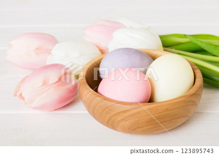 Happy Easter composition. Easter eggs in basket on colored table with yellow Tulips. Natural dyed colorful eggs background with copy space 123895743