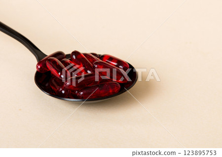 Vitamin capsules in a spoon on a colored background. Pills served as a healthy meal. Red soft gel vitamin supplement capsules on spoon 123895753