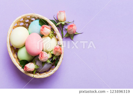 Happy Easter. Easter eggs in basket on colored table with yellow roses. Natural dyed colorful eggs background top view with copy space Happy Easter. Easter eggs in basket on colored table with yellow roses. Natural dyed colorful eggs background top view with copy space 123896319